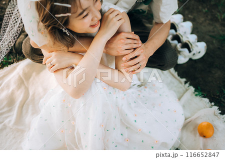 ピクニックをしながら前撮り撮影をする新郎新婦、後ろからハグ ピクニックをしながら前撮り撮影をする新郎新婦、後ろからハグ 116652847