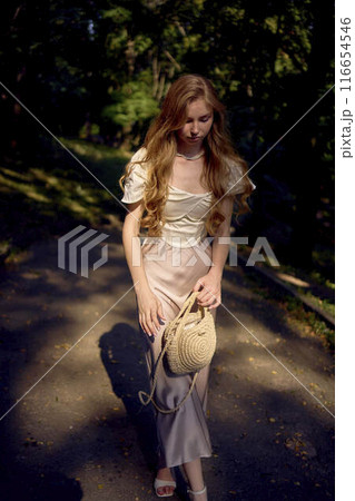 beautiful teenage girl in a silk skirt and a corset in the old money style walks in the park and along the river bank 116654546