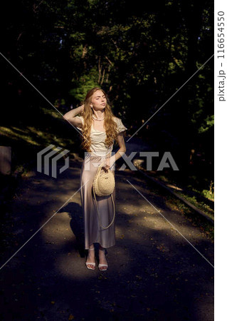 beautiful teenage girl in a silk skirt and a corset in the old money style walks in the park and along the river bank 116654550