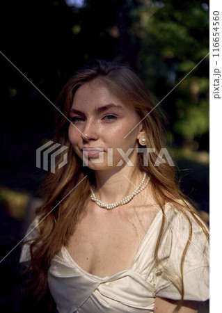 beautiful teenage girl in a silk skirt and a corset in the old money style walks in the park and along the river bank 116654560