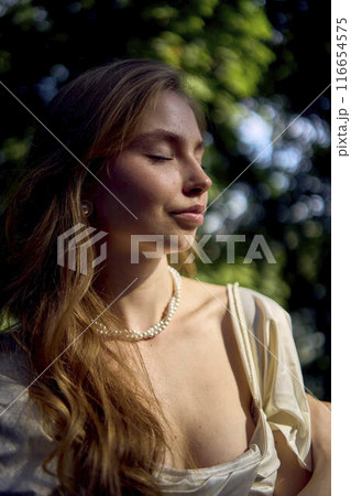 beautiful teenage girl in a silk skirt and a corset in the old money style walks in the park and along the river bank beautiful teenage girl in a silk skirt and a corset in the old money style walks in the park and along the river bank 116654575
