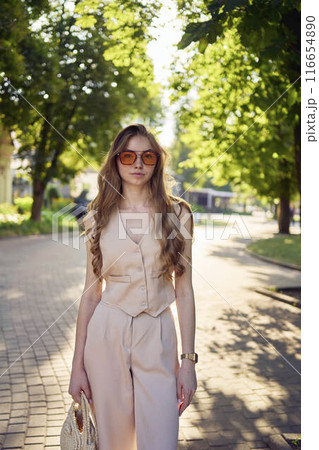 a beautiful teenage girl in a peach fuzz suit with a waistcoat, in the old money style  walks through the morning city 116654890