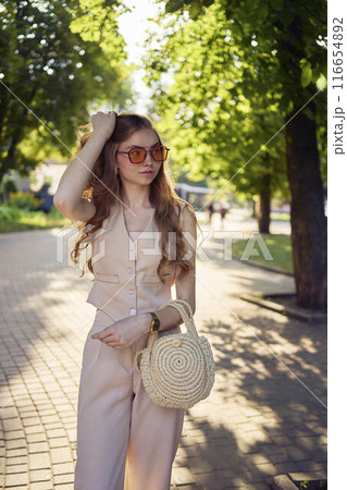 a beautiful teenage girl in a peach fuzz suit with a waistcoat, in the old money style  walks through the morning city 116654892
