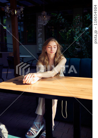 a  beautiful teenage girl in a peach fuzz suit with a vest, in the old money style in a fancy restaurant 116654984