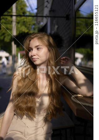 a  beautiful teenage girl in a peach fuzz suit with a waistcoat in the old money  style sits at the bar outside 116655121