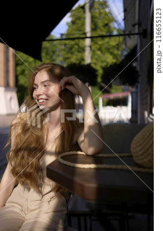 a  beautiful teenage girl in a peach fuzz suit with a waistcoat in the old money  style sits at the bar outside 116655123