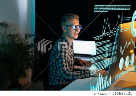 Smiling Man Analyzing Data on Computer Screen in Office 116656120