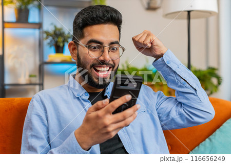 Surprised excited Indian man use smartphone reading good news amazed by online bet bid game win Surprised excited Indian man use smartphone reading good news amazed by online bet bid game win 116656249