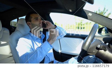 Male entrepreneur speaking by smartphone during riding on electrical auto with autopilot at urban road. Confident businessman talking on phone while riding an autonomous self driving electric car Male entrepreneur speaking by smartphone during riding on electrical auto with autopilot at urban road. Confident businessman talking on phone while riding an autonomous self driving electric car 116657179