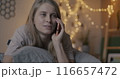 Pretty young lady chatting on mobile phone discussing news smiling lying in bed in illuminated bedroom in evening. People and cellphone communication concept. 116657472