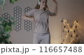 Happy young woman dancing on bed listening to music with headphones having fun in bedroom in evening. Leisure activity and youth lifestyle concept. 116657488