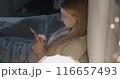 Young lady using smartphone messaging sitting in bed in dark bedroom at sleepless night. Modern technology and online communication concept. 116657493