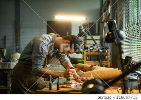Focused craftsman intently working on a leather project in his local workshop Focused craftsman intently working on a leather project in his local workshop 116657715