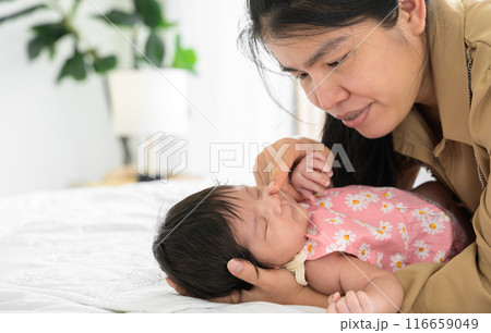 Asian mother touching nose of newborn baby daughter on bed at home. Infant girl sleeping on mom arm. Love and new life concept 116659049