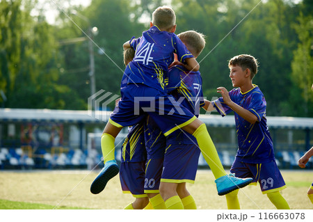 Dynamic moment of victory. Boys, friends in blue uniform, soccer players in motion, jumping and hugging, celebrating winning game. Dynamic moment of victory. Boys, friends in blue uniform, soccer players in motion, jumping and hugging, celebrating winning game. 116663078