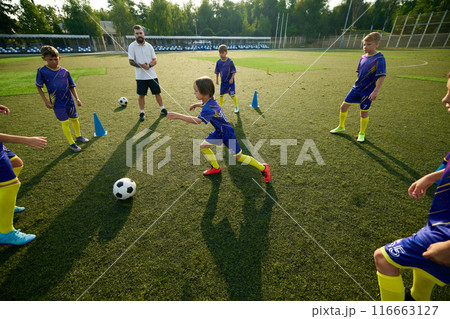 Boy, child, soccer player navigating ball through field, while coach providing instruction and support. Outdoor football game 116663127