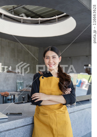 Smiling Barista in Yellow Apron Standing in Modern Industrial Style Coffee Shop 116663628