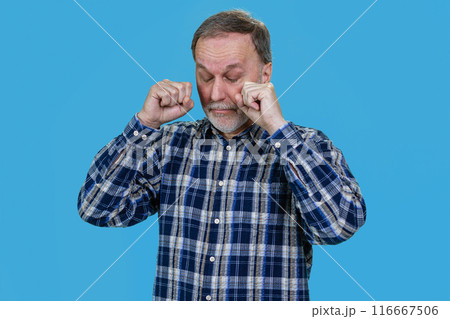 Portrait of crying senior man wiping his tears. Isolated on blue. Portrait of crying senior man wiping his tears. Isolated on blue. 116667506