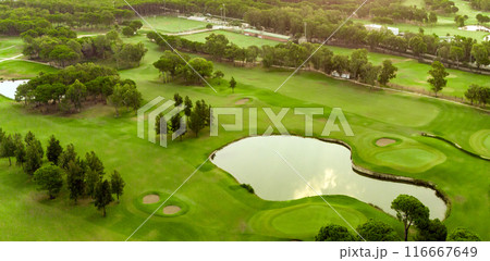 Golf course at sunset with pond and sand traps. Scenic panoramic view of golf fairway with bunkers. Golf field with pines 116667649