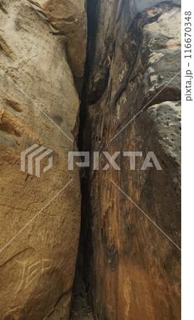 A narrow crack separates two large sandstone cliff faces. Vertical mobile photo. sstkvertical 116670348