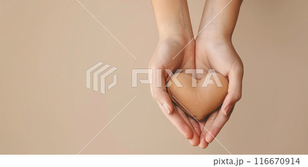 Hands cupped around a brown heart against a tan background with copy space. Generative AI 116670914
