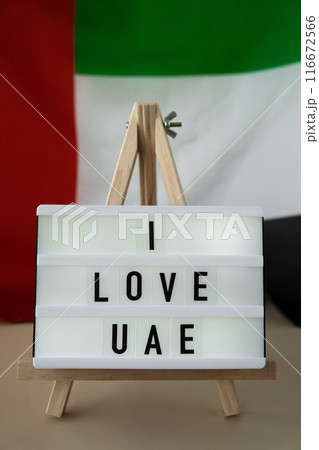 Lightbox with text I LOVE UAE on background of waving UAE flag made from silk. United Arab Emirates flag with concept of tourism and traveling. Inviting greeting card, advertisement 116672566
