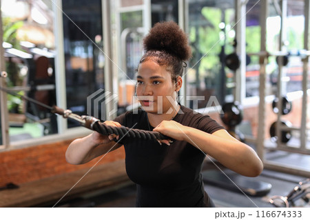 Healthy strong female African American plus-size lifts weights exercise in gym. 116674333