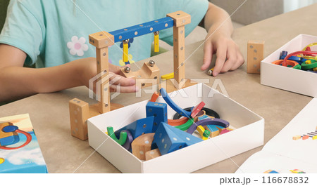 Girl assembles swing from magnetic wooden construction set. Toys and activiti children. Developmental activities at home.  116678832