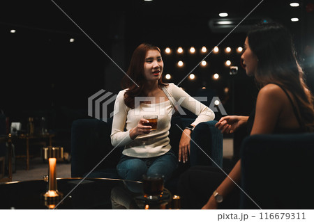 Pretty young woman talking with her friend and enjoying drinks at luxury night club Pretty young woman talking with her friend and enjoying drinks at luxury night club 116679311