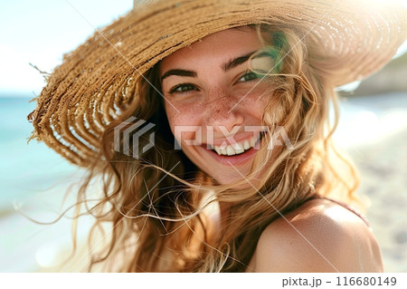 A woman with a straw hat smiles happily on the sunny beach landscape 116680149