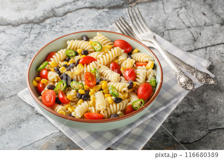 Fresh homemade colorful vegan fusilli pasta salad with beans, corn, tomato and jalapeno close-up in a plate. Horizontal 116680389