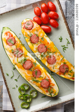 Healthy Zucchini Pizza with cheddar and mozzarella cheese, sausages, tomato sauce and spices close-up in a plate on the table. Vertical top view 116680399