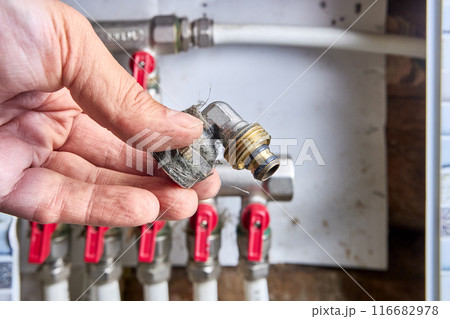 Fitting brass pipe angle adapter with transition to external thread in hand of plumber who is repairing manifold in house. 116682978