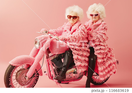 Two stylish grandmothers dressed in pink crochet outfits, sitting on a crochet-covered motorcycle Two stylish grandmothers dressed in pink crochet outfits, sitting on a crochet-covered motorcycle 116683619
