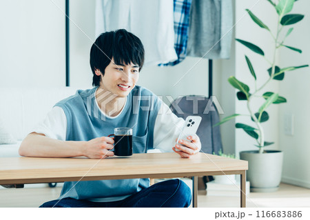 リビングでスマホを見る若い男性　 116683886