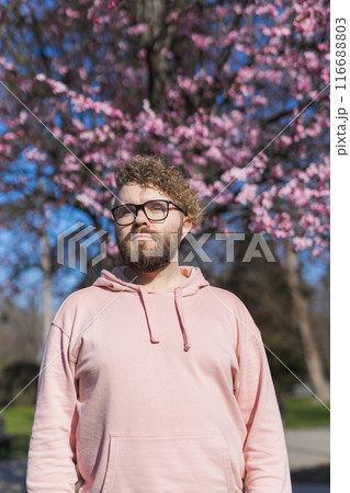 Man allergic enjoying after treatment from seasonal allergy at spring. Portrait of happy bearded man smiling in front of blossom tree at springtime. Spring blooming and allergy concept. Copy space 116688803