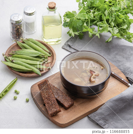 Pea soup with smoked meat in a bowl on a wooden board with croutons, fresh vegetables, herbs  116688855