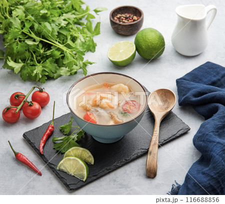 Tom yam soup with shrimp and chili pepper in a blue bowl on a light background with fresh vegetables Tom yam soup with shrimp and chili pepper in a blue bowl on a light background with fresh vegetables 116688856