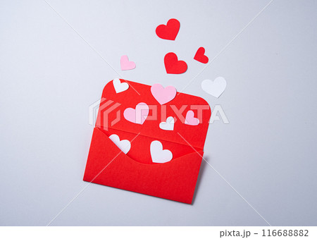 Red, pink and white paper hearts fly out of the red envelope on gray background. 116688882