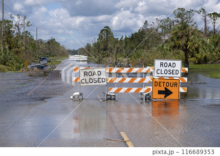 Flooded street in Florida after hurricane rainfall with road closed signs blocking driving of cars. Safety of transportation during natural disaster concept 116689353