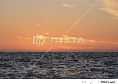 Dramatic bright red sky at ocean sunset, soft evening clouds over sea dark water 116689388
