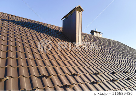Closeup snow guard for safety in winter on house roof top covered with steel shingles. Tiled covering of building 116689456