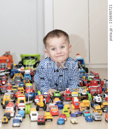 Concept of children's toys. A little boy, 4 years old, plays happily, lying on the floor, with colorful small and large cars in the children's room. 116690721