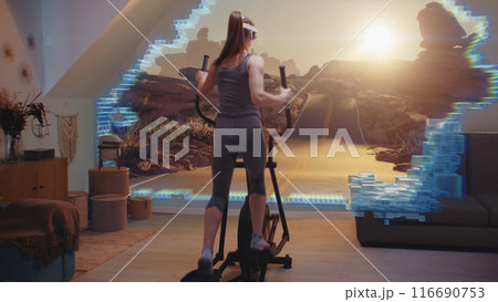 Female athlete in AR headset trains on orbitrek. Virtual reality screen with nature landscape Female athlete in AR headset trains on orbitrek. Virtual reality screen with nature landscape 116690753