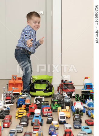 Children. Toy cars. A small cheerful and handsome boy, 4 years old, wearing a checkered shirt, plays with many colorful cars in a home interior. 116690756