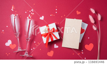 Flat lay of celebration. Two glasses, a gift box, a craft letter, flowers, paper hearts and confetti 116691446
