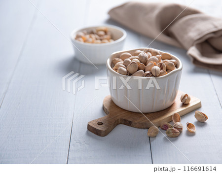 Pistachio nuts in a white bowl on a light wooden background. Front view and copy space 116691614