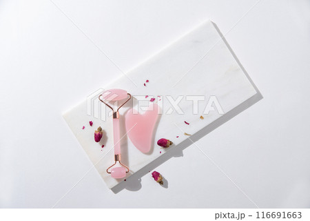 flat lay with pink gua sha for face massage and dry roses on white background with hard shadows.  116691663