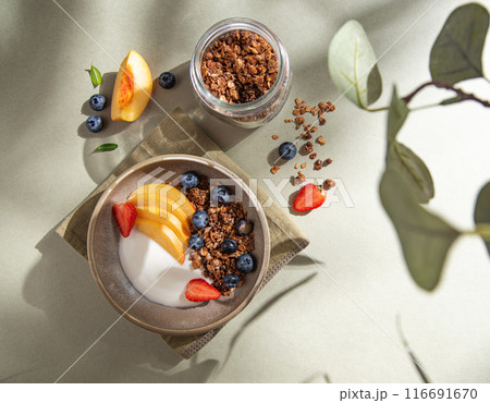 Delicious natural yogurt with homemade granola, peach, berries in a bowl and jar with muesli  116691670