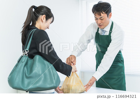 レジで会計する女性客とお弁当を渡す男性コンビニ店員 116694321